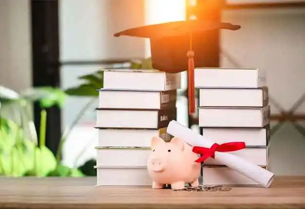 Graduation robe hat placed over a stack of books beside piggy bank