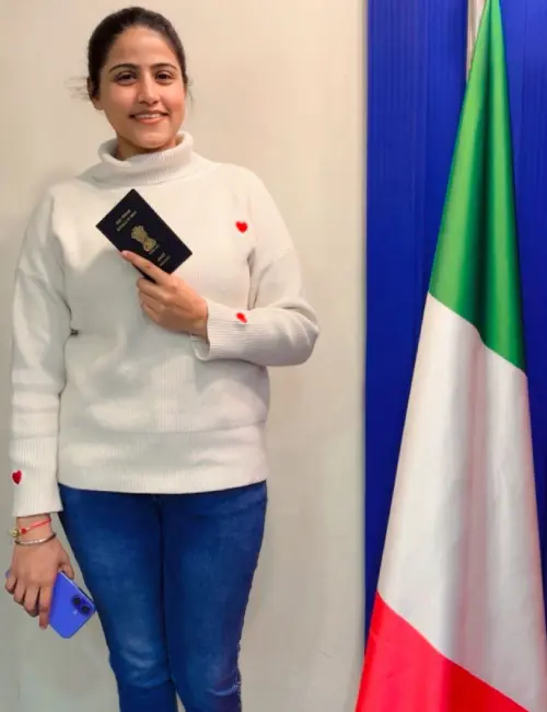 Navjeet Kaur stands beside the Italian flag, holding her passport